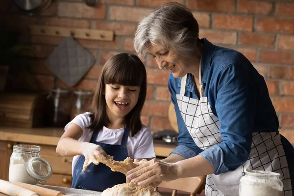Alegre nieta niño ayudando feliz abuela a amasar masa —  Fotos de Stock