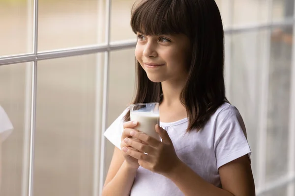 Happy cute przemyślane dziewczyna pije mleko, trzymając szkło — Zdjęcie stockowe