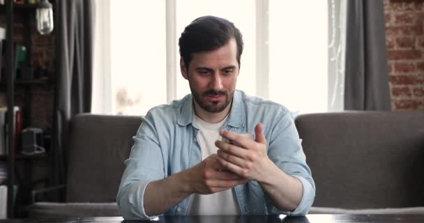 Hombre sosteniendo mensajes de escritura de teléfonos inteligentes sentado en el escritorio del lugar de trabajo — Vídeos de Stock
