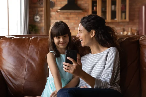 Веселая мама показывает смартфон счастливой маленькой дочке — стоковое фото