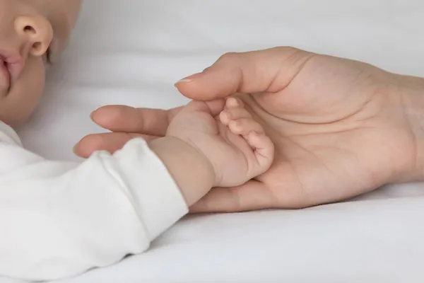 Возделывайте крупным планом любящую мать трогающую маленькую руку ребенка — стоковое фото