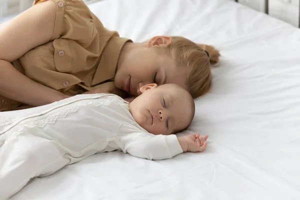 Закройте усталую заботливую мать с ребенком, спящим на кровати — стоковое фото