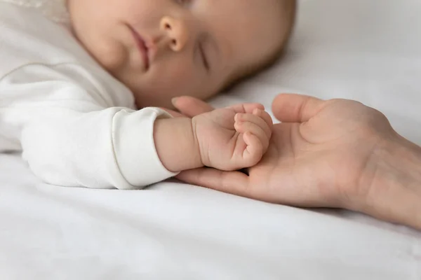 De cerca amorosa madre sosteniendo durmiendo pequeña mano de bebé —  Fotos de Stock