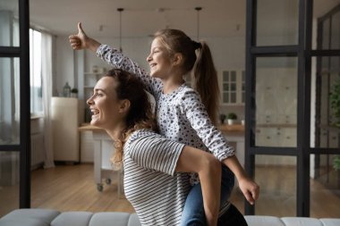 Neşeli genç bir anne sırtına yaslanıp gülüyor küçük kız çocuğu..