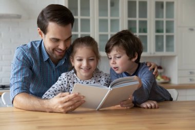 Mutlu genç baba küçük çocuklara kağıt kitap okuyor..