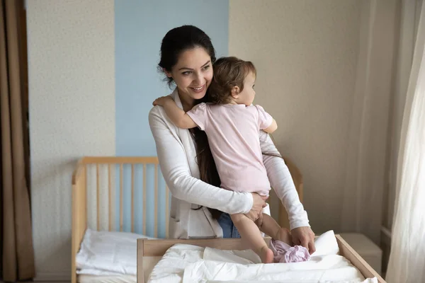 Leende omtänksam ung mor byta baby kläder, blöja på bordet — Stockfoto