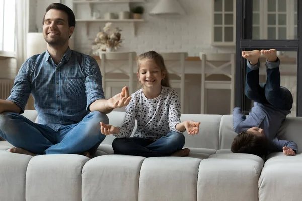 Pai feliz praticando ioga com a filha pequena, enquanto o filho jogando. — Fotografia de Stock