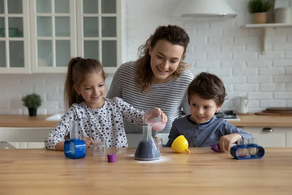 Feliz madre joven y cuidadosa ayudando a los niños pequeños a hacer experimentos químicos. —  Fotos de Stock