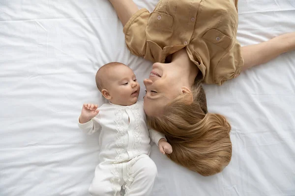Вид сверху на любящую молодую мать и ребенка, лежащего на кровати — стоковое фото
