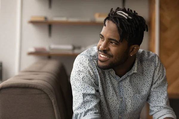 Happy young african ethnicity man dreaming resting on sofa. — Stock Photo, Image