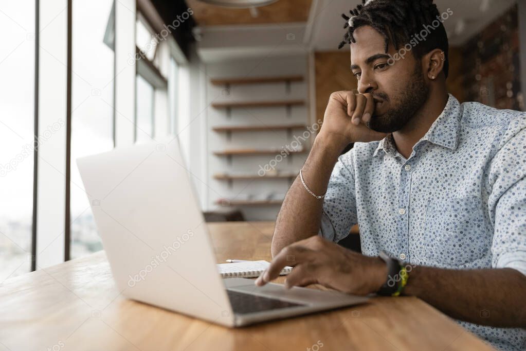 Pensive millennial african american man working on computer.