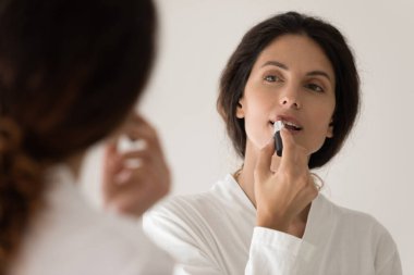 Bornozlu kadın dudaklarına ruj sürüyor.