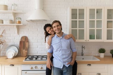 Karısı kocasını kucaklıyor, kameraya bakıyor, rahat bir mutfakta dinleniyor.