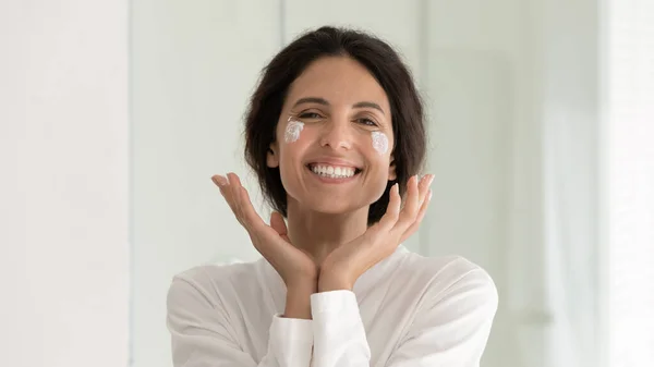 Bella donna applicare la crema sulle guance sorriso guardare la fotocamera — Foto Stock