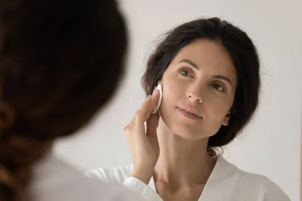 Vrouw kijkt in spiegel houdt katoen schijf reinigen gezicht huid — Stockfoto