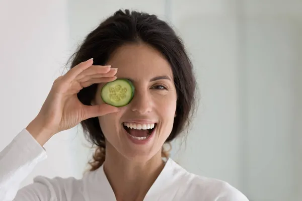 Vrouw houden komkommer slice cover oog, glimlach kijk naar de camera — Stockfoto