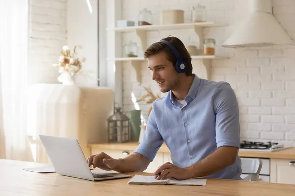 El hombre utiliza el ordenador portátil notando información en el copybook e-learning en casa —  Fotos de Stock