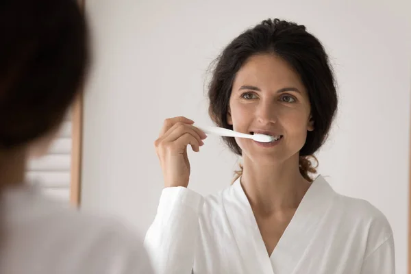 Young woman brush her teeth standing in front of mirror — Stock Photo, Image