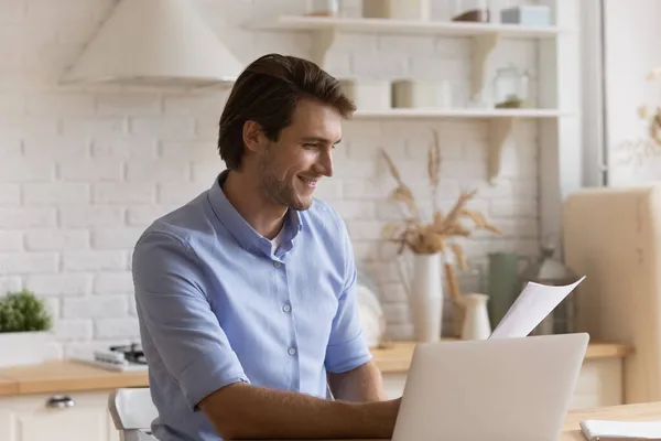 Mann sitzt mit Laptop am Tisch und hält Dokumente bereit — Stockfoto