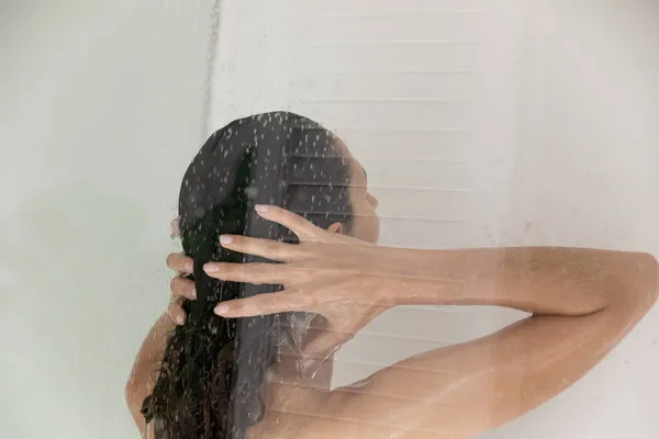 女性はシャワーで流れる水の下に立って髪を洗う — ストック写真
