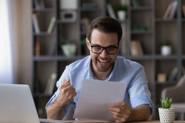 Başarıyı kutlayan neşeli genç adam, kağıt mektup okuyor..