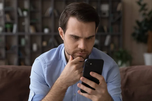 Thoughtful young man looking at cellphone screen. — Stock Photo, Image