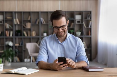 Gülümseyen yakışıklı genç adam cep telefonu uygulamalarını kullanıyor..