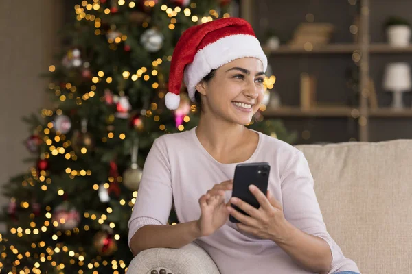 Dreamy smiling millennial Indian woman using cellphone. — Stock Photo, Image