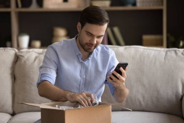 Mutlu genç adam paketleri açıyor, gezici uygulamayla gözden geçiriyor..