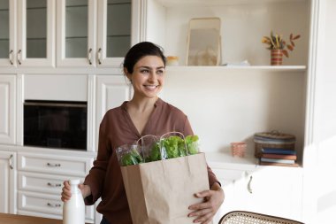 Mutfakta elinde alışveriş torbalarıyla bekleyen bir kadın.