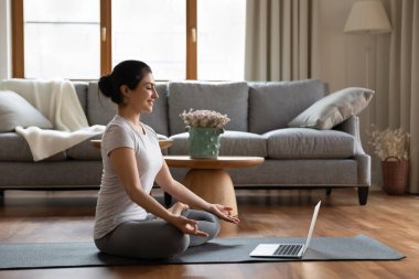 Hintli kadın evde online antrenörle meditasyon yapıyor.