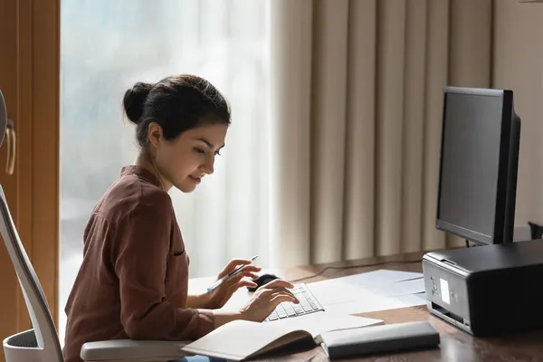 Mujer india estudiando sentada en el escritorio comprobar la información en el bloc de notas —  Fotos de Stock