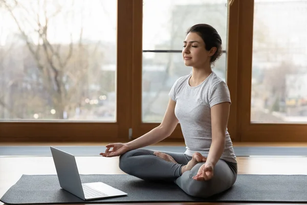 Serene Indian woman do meditation practise sit cross-legged on mat