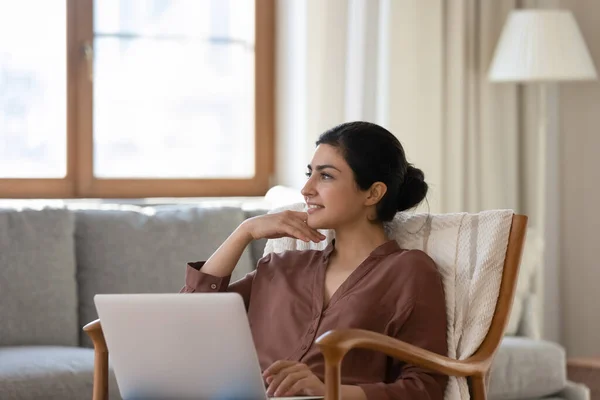 Femme relaxant sur fauteuil avec ordinateur portable regardant dans la distance rêverie — Photo