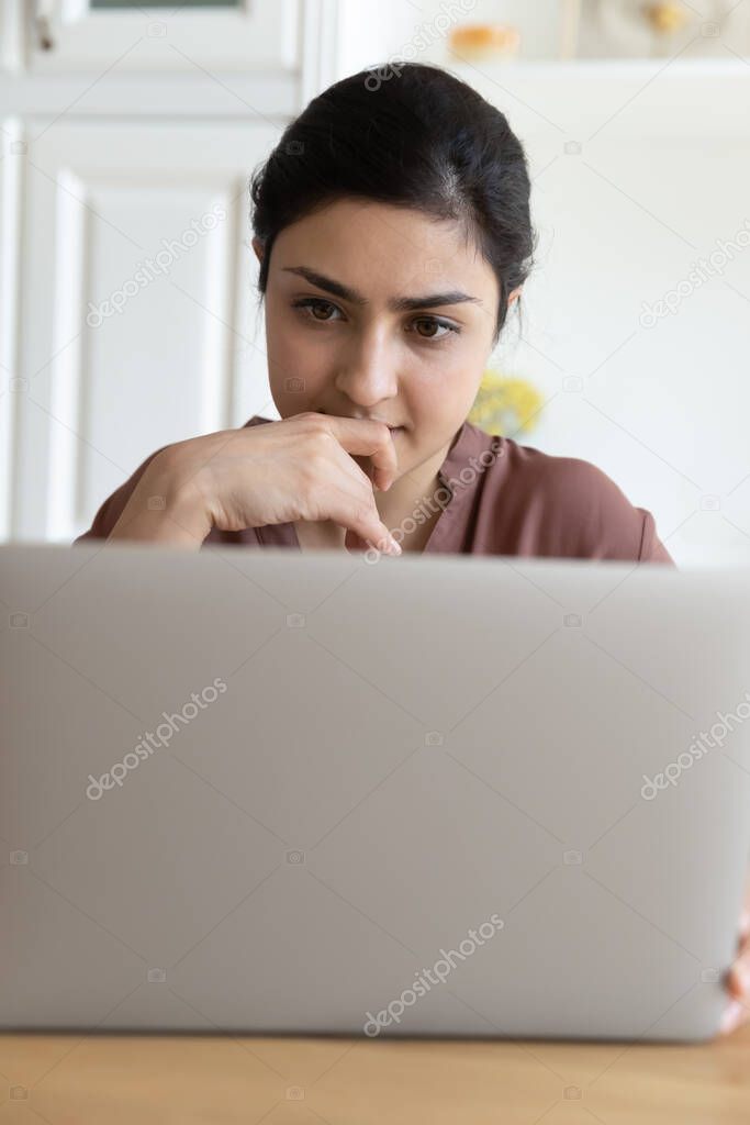 Serious Indian woman working studying on laptop, vertical image