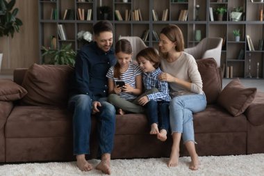 Çocuklu mutlu bir aile akıllı telefon kullanıyor, kanepede oturuyor.
