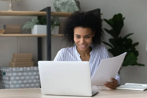 微笑着持有文件的非洲裔美国女商人，在笔记本电脑上工作 — 图库照片