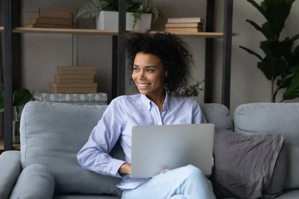 Drömmande leende afroamerikansk kvinna håller laptop, tittar på avstånd — Stockfoto