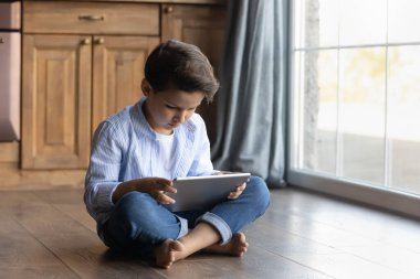 Ergen çocuk dokunmatik blogla meşgul bir şekilde yerde oturuyor.