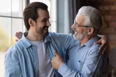 Gururlu yaşlı baba yetişkin oğlanı kucaklıyor başarıyla kutluyor.