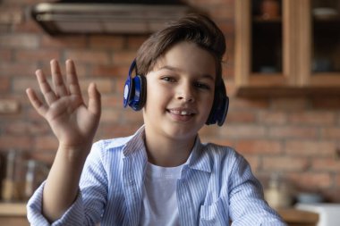 Ortaokul öğrencisi kulaklıklı çocuk web kamerasına el sallıyor.