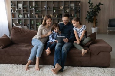 Çocuklu mutlu bir aile tablet kullanıyor, kanepede dinleniyor.