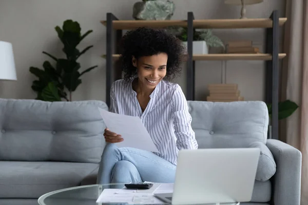 Sorrindo mulher afro-americana trabalhando com documentos financeiros, usando laptop — Fotografia de Stock