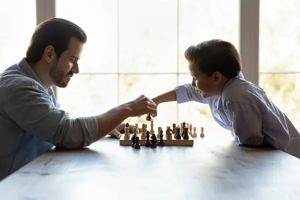 Молодой взрослый отец-одиночка играет в шахматы с сыном-подростком — стоковое фото