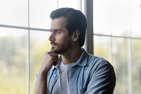 Pensive millennial bearded guy stand by window look at distance — Stock Photo, Image