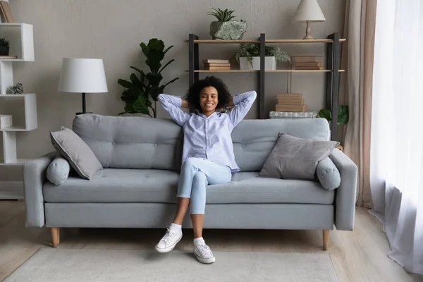 Full length smiling relaxed African American woman resting on couch — Stock Photo, Image