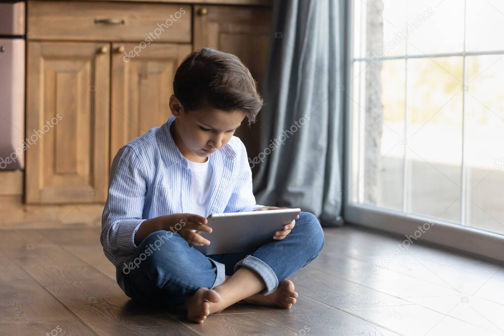 Tween boy sit on floor engaged in blogging on touchpad