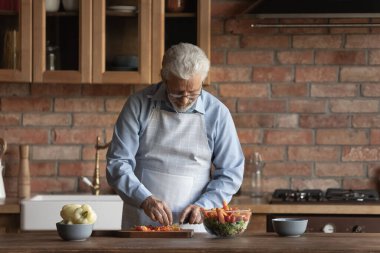 Yaşlı adam mutfakta ev yapımı salata için sebze doğradı.