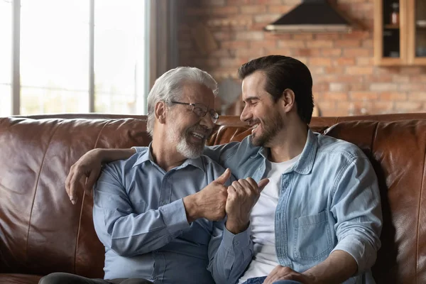 Fericit pensionar tata tânăr fiu stând pe canapea îmbrățișare vorbind — Fotografie, imagine de stoc