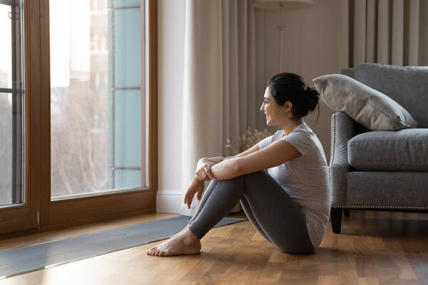 Indian woman in sportswear relax after workout looks out window